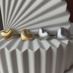 Vidéo des boucles d'oreilles "S'aimer", en maxi cœurs dorés et argentés mat, en acier Inoxydable, posées sur un fond beige texturé.