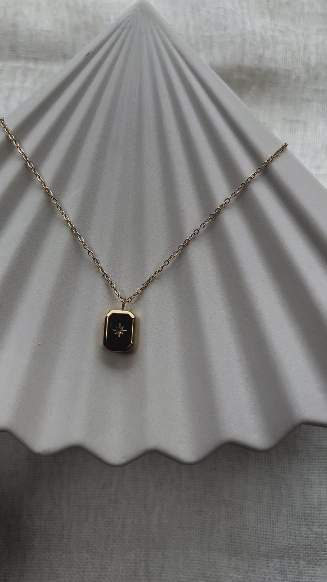 Vidéo du collier "Ma voie" avec pendentif rectangulaire personnalisable en acier doré, sur fond beige texturé.