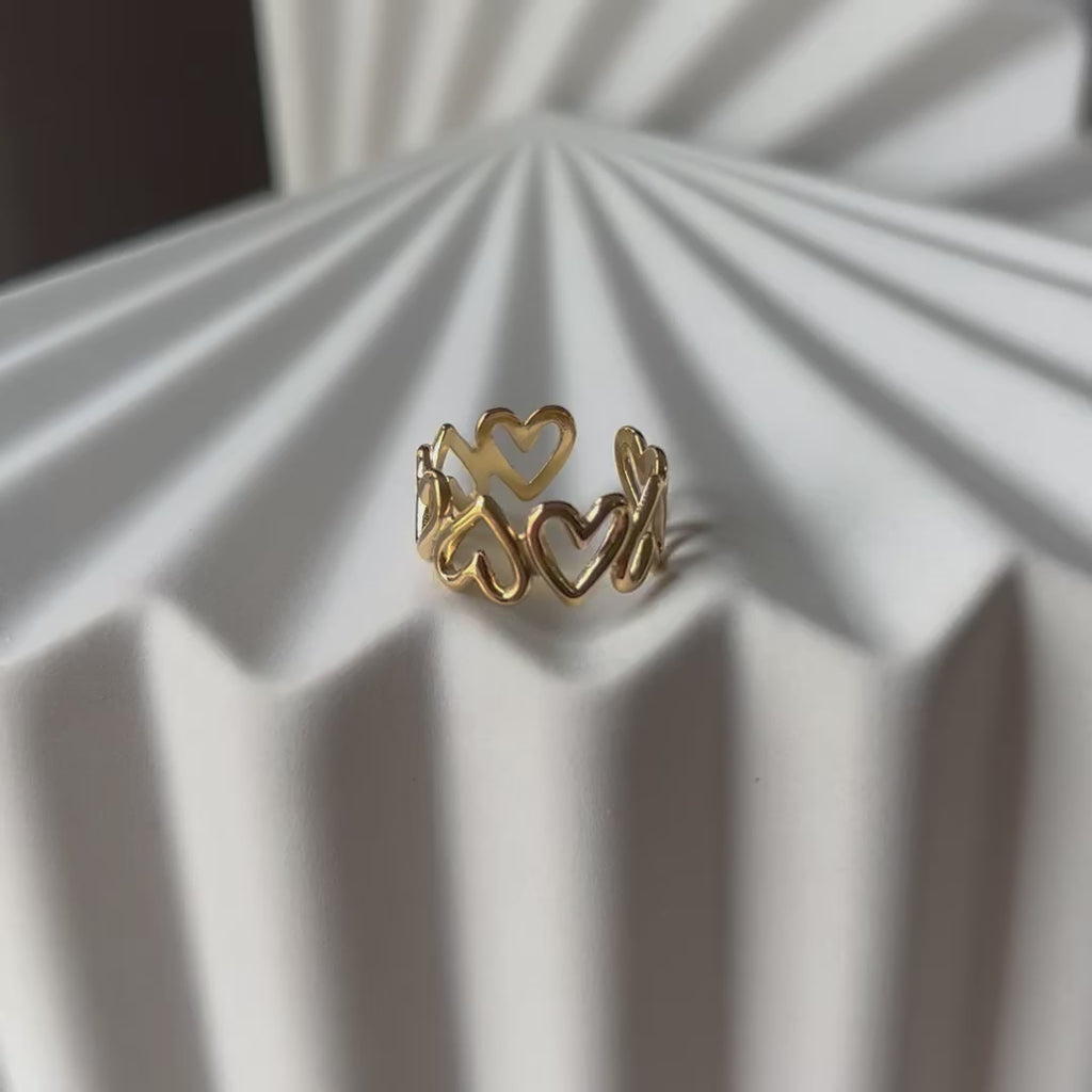 Vidéo de la bague ajustable Mon message, en acier inoxydable doré, orné de cœurs, posée en gros plan sur un support texturé beige clair.