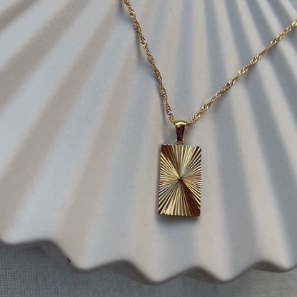 Vidéo du collier Résilience en acier doré avec pendentif rectangulaire gravé de rayons, personnalisable au verso.