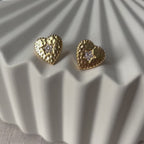 Vidéo des boucles d'oreilles Promesse, en forme de cœur ornées d'une étoile, en acier inoxydable doré, posées sur un support beige texturé.