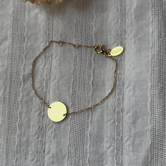Vidéo du bracelet "Confiance" en acier doré personnalisable avec médaille ronde, présenté sur un tissu beige texturé. 
