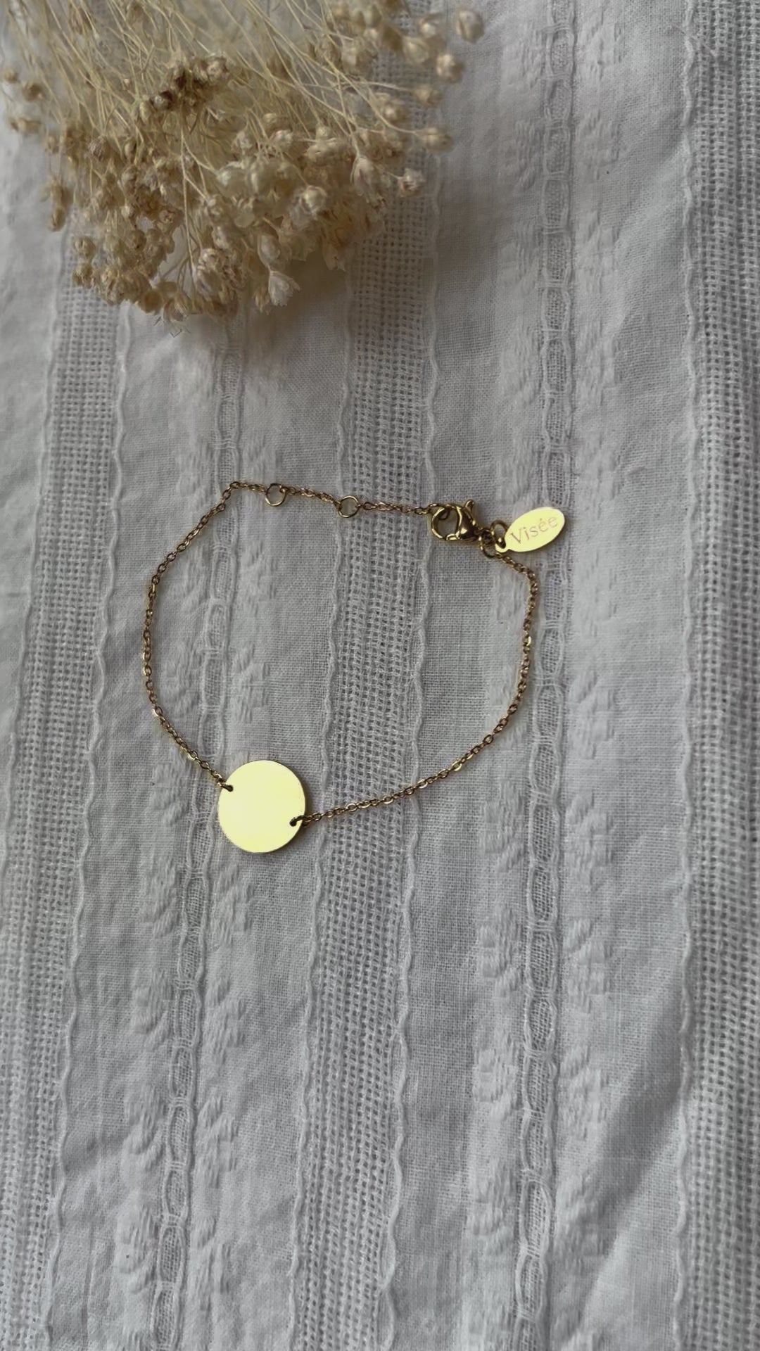 Vidéo du bracelet "Confiance" en acier doré personnalisable avec médaille ronde, présenté sur un tissu beige texturé. 