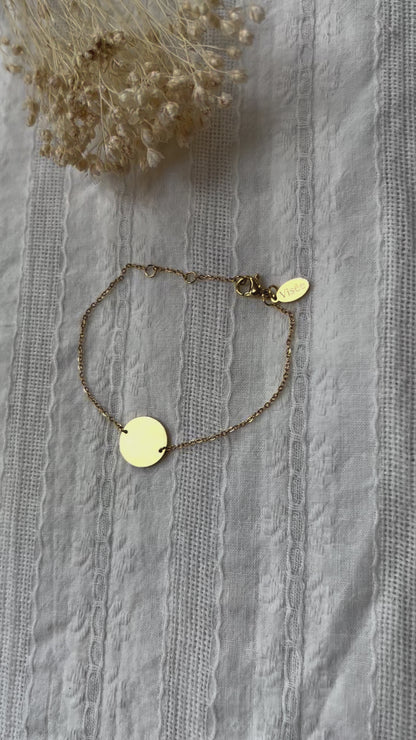 Vidéo du bracelet "Confiance" en acier doré personnalisable avec médaille ronde, présenté sur un tissu beige texturé. 