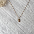 Vidéo du collier "Ma vérité" avec pendentif rectangulaire personnalisable en acier doré, présenté sur un fond beige texturé.