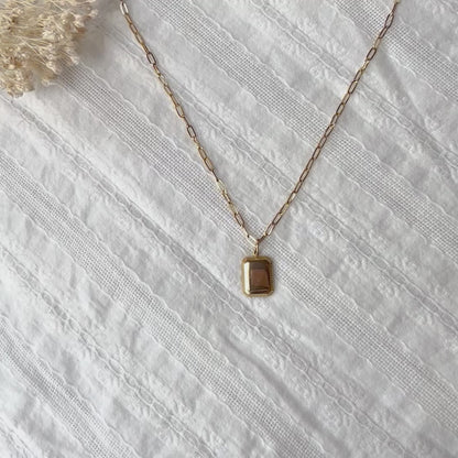 Vidéo du collier "Ma vérité" avec pendentif rectangulaire personnalisable en acier doré, présenté sur un fond beige texturé.