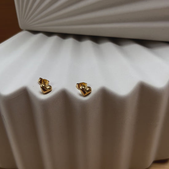 Vidéo des boucles d'oreilles "Tendre discrétion" de Visée, en forme de cœur en acier doré, posées sur un fond beige texturé.