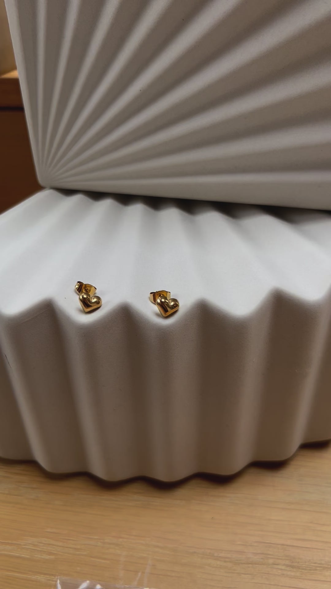 Vidéo des boucles d'oreilles "Tendre discrétion" de Visée, en forme de cœur en acier doré, posées sur un fond beige texturé.