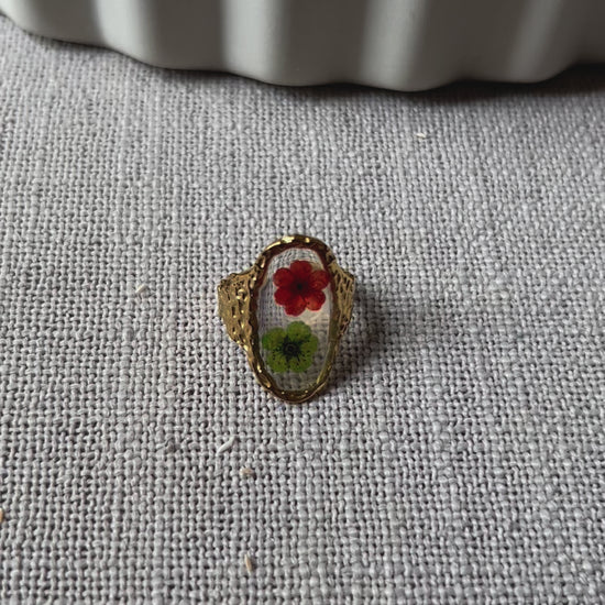 Vidéo de la bague ajustable Mon rythme, en acier inoxydable doré, ornée de deux fleurs séchées rouge et verte.
