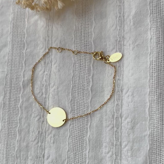 Vidéo du bracelet "Confiance" en acier doré personnalisable avec médaille ronde, présenté sur un tissu beige texturé. 