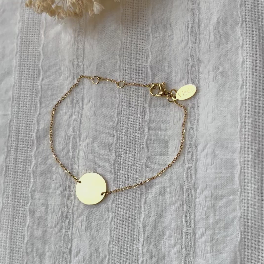 Vidéo du bracelet "Confiance" en acier doré personnalisable avec médaille ronde, présenté sur un tissu beige texturé. 
