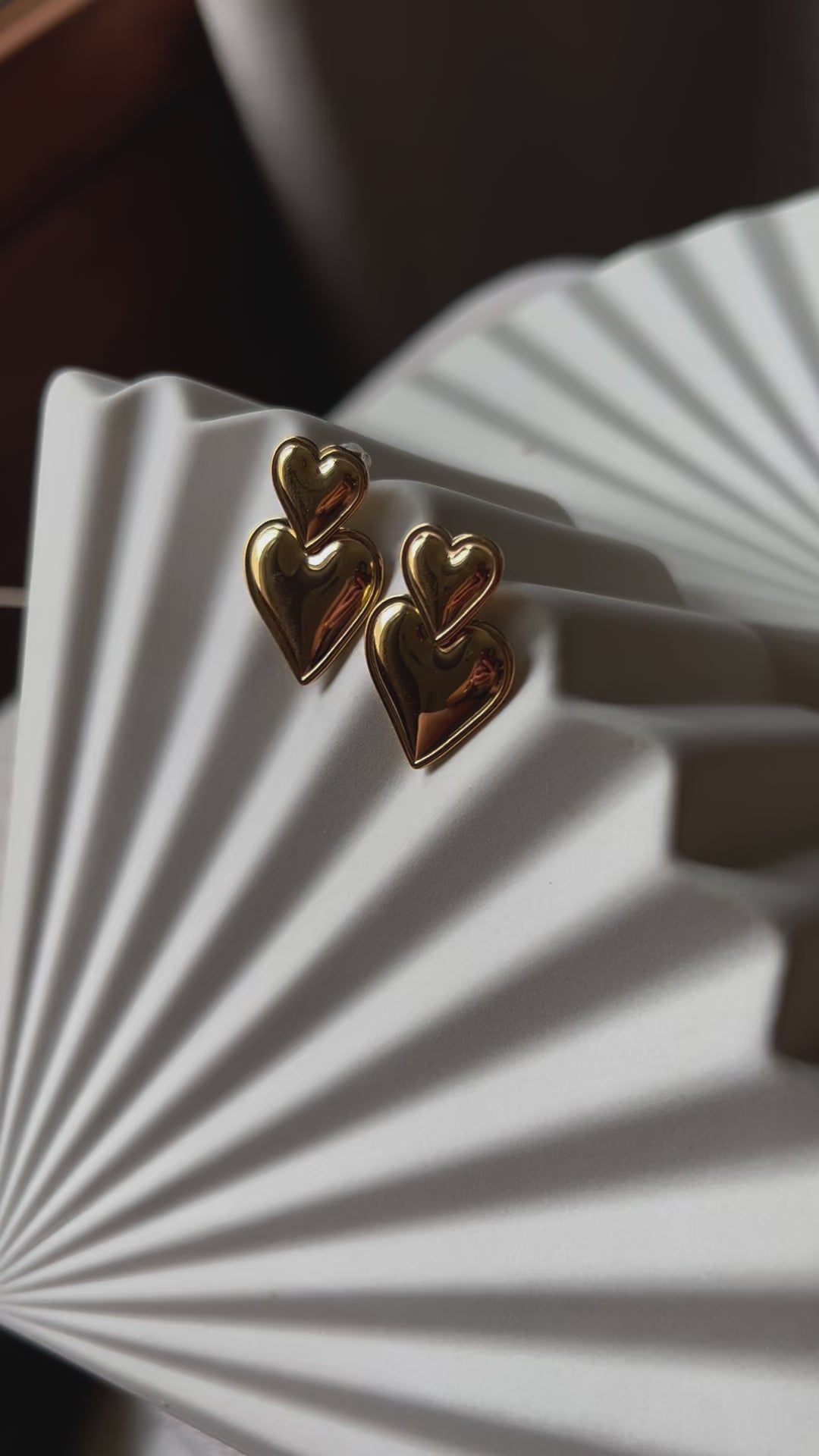 Vidéo des boucles d'oreilles "Elle m'a dit" en forme de double coeur, en acier. Posées sur un fond beige texturé. 