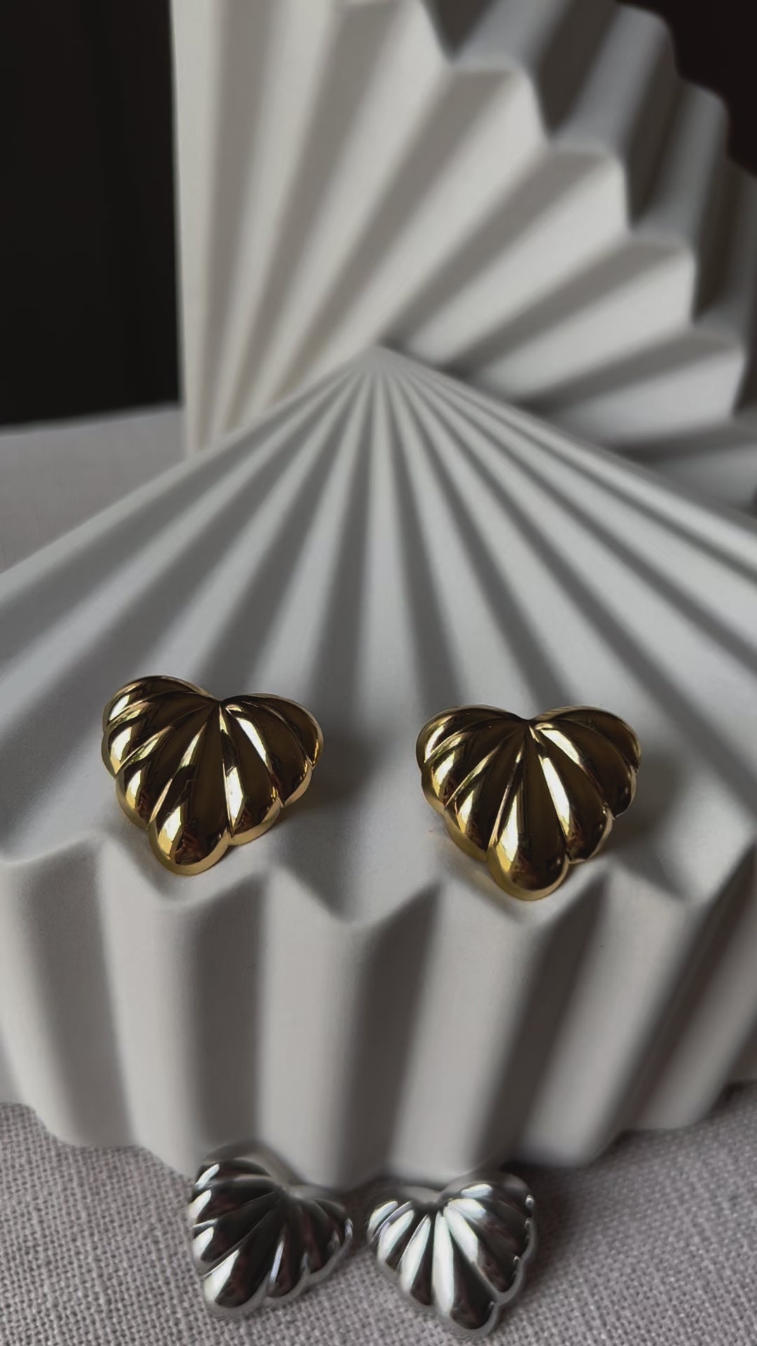 Vidéo des boucles d'oreilles "Coeur audacieux", en acier inoxydable, au design en relief en forme de coeur, posées côte à côte sur un fond beige texturé.