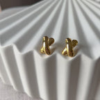 Vidéo des boucles d'oreilles "Révèle toi", au design croix en acier inoxydable doré, photographiées sur un fond beige texturé.