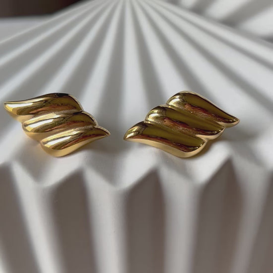 Vidéo des boucles d'oreilles Elan doux en forme d'ailes, en acier inoxydable doré, posé sur support blanc texturé