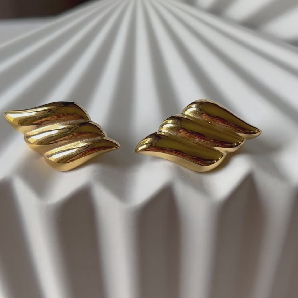 Vidéo des boucles d'oreilles Elan doux en forme d'ailes, en acier inoxydable doré, posé sur support blanc texturé