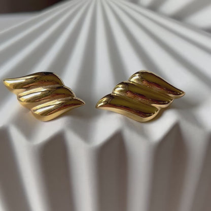 Vidéo des boucles d'oreilles Elan doux en forme d'ailes, en acier inoxydable doré, posé sur support blanc texturé