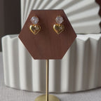 Vidéo des boucles d'oreilles Intuition en acier doré, coeur délicat serti de pierre scintillante, présentées sur un socle.