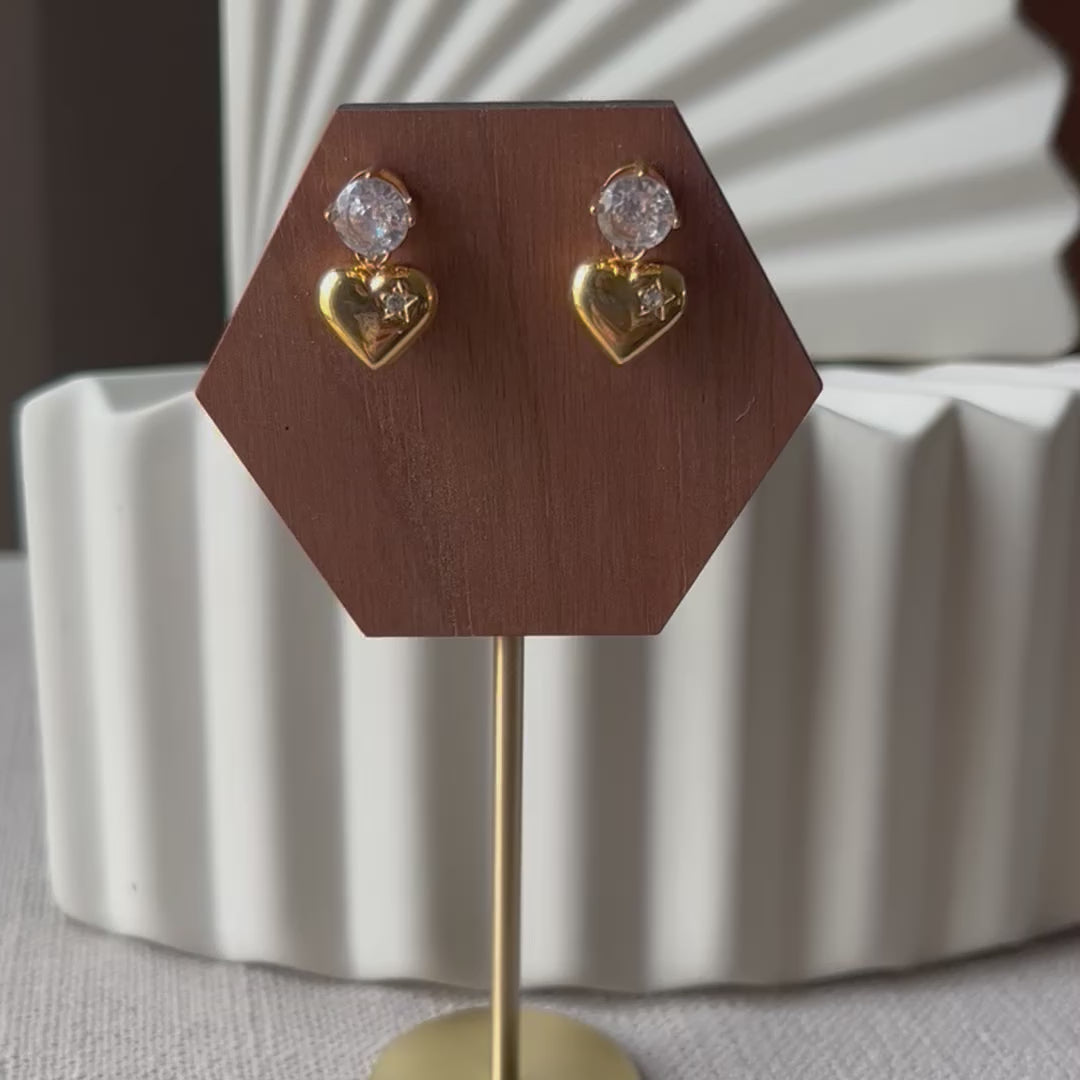Vidéo des boucles d'oreilles Intuition en acier doré, coeur délicat serti de pierre scintillante, présentées sur un socle.