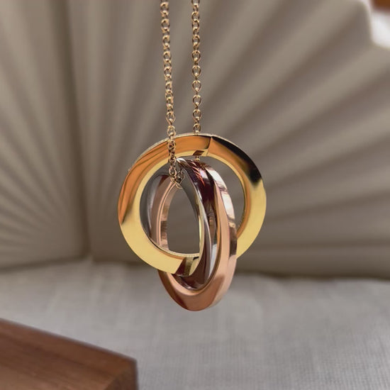 Vidéo du collier "Je deviens" en acier inoxydable, avec trois cercles entrelacés personnalisables, posé sur un fond beige texturé.