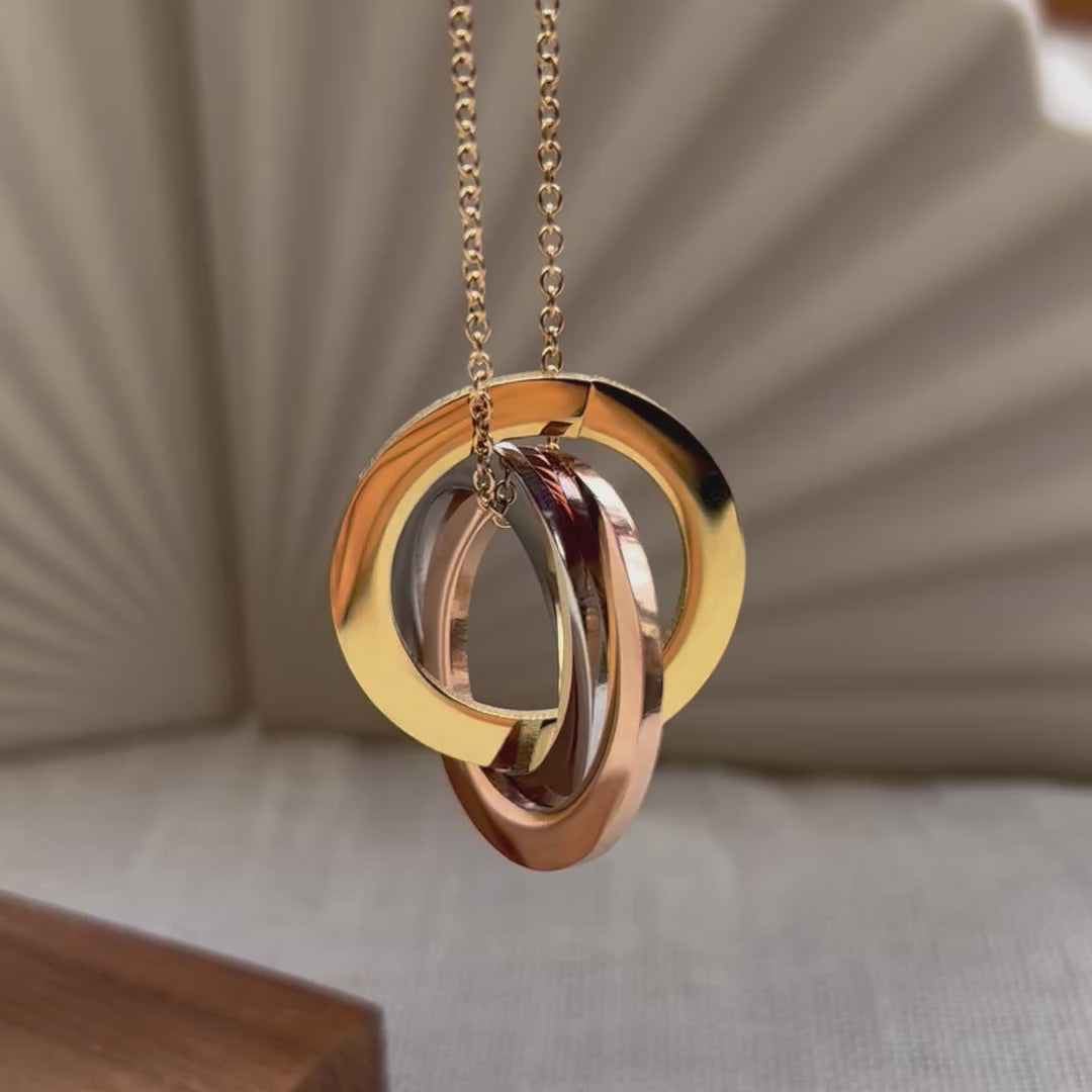 Vidéo du collier "Je deviens" en acier inoxydable, avec trois cercles entrelacés personnalisables, posé sur un fond beige texturé.