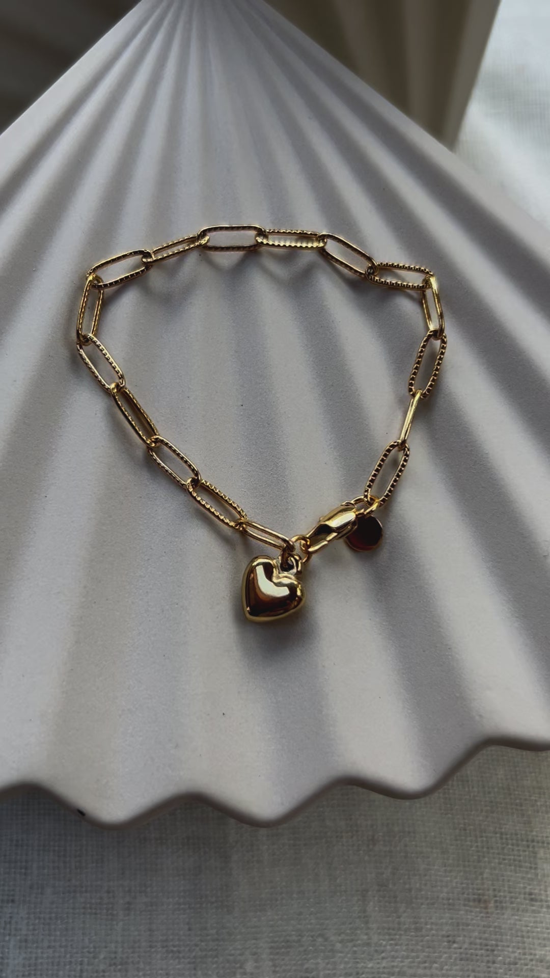 Vidéo du bracelet Valeur acier inoxydable doré, avec breloque cœur personnalisable, posé sur un fond beige texturé.
