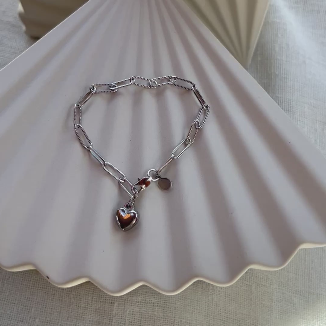 Vidéo du bracelet Valeur acier inoxydable argenté, avec breloque cœur personnalisable, posé sur un fond beige texturé.