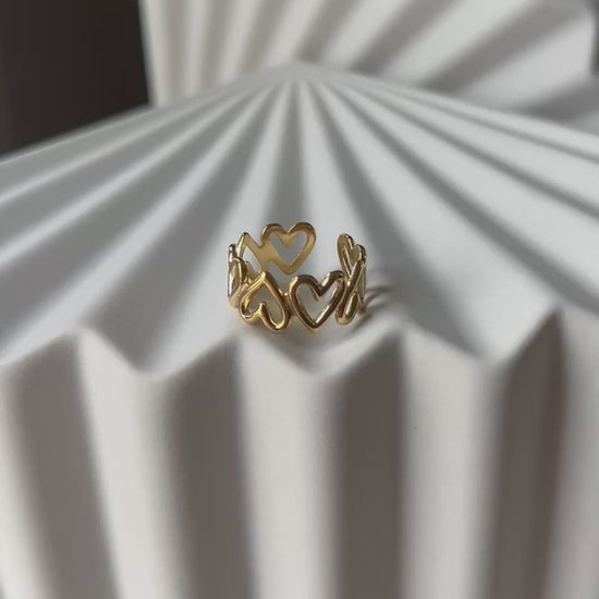 Vidéo de la bague ajustable Mon message, en acier inoxydable doré, orné de coeurs, posée en gros plan sur un support texturé beige clair.