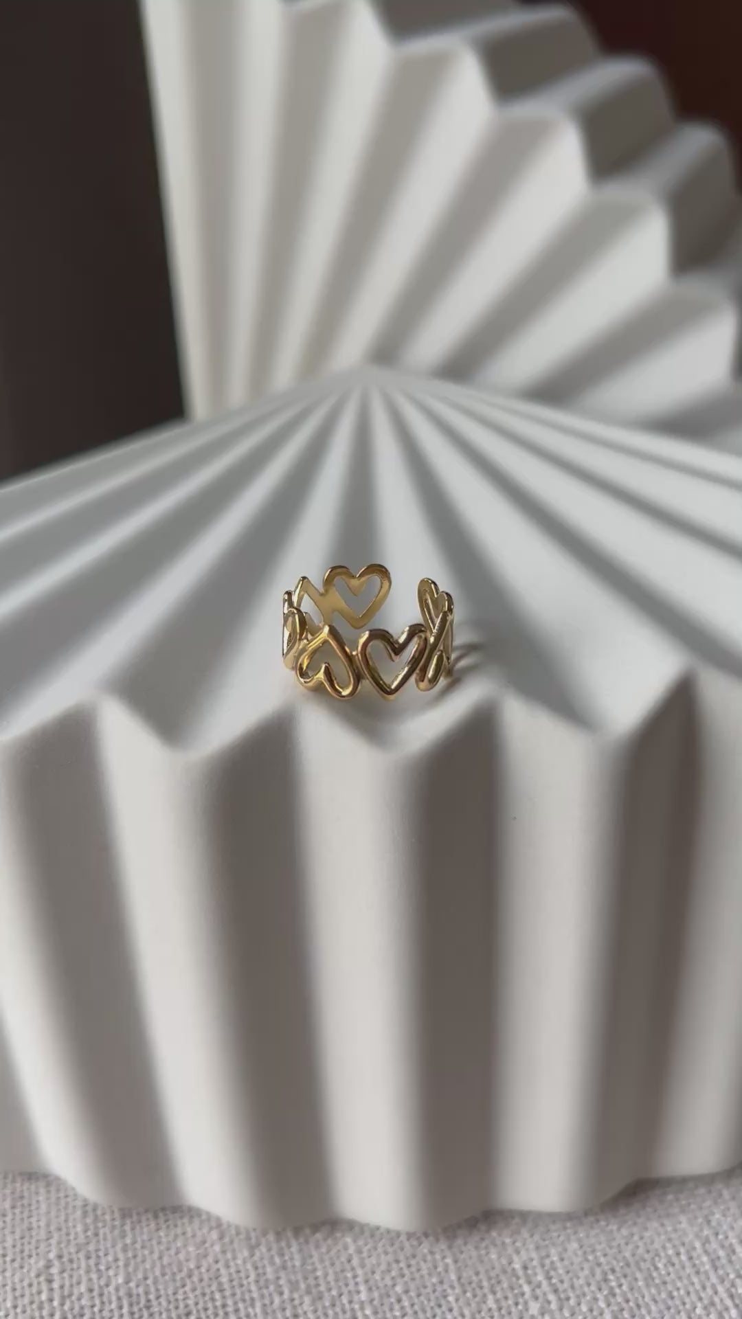 Vidéo de la bague ajustable Mon message, en acier inoxydable doré, orné de coeurs, posée en gros plan sur un support texturé beige clair.