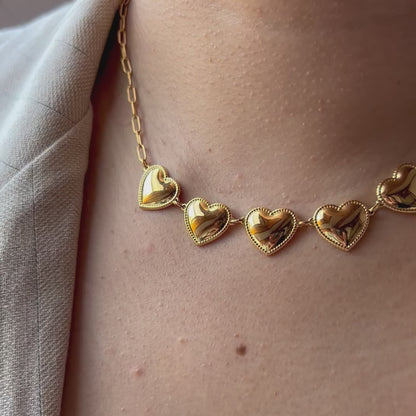 Vidéo du collier "Je suis là" de Visée, composé de cœurs personnalisables en acier doré, posé sur un fond beige texturé.