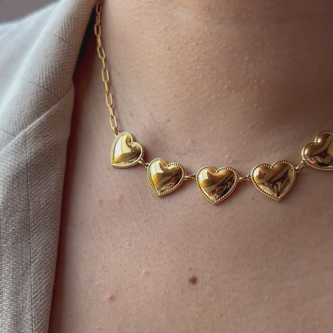 Vidéo du collier "Je suis là" de Visée, composé de cœurs personnalisables en acier doré, posé sur un fond beige texturé.