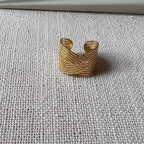 Vidéo de la bague Avenir ajustable, au design géométrique en acier inoxydable doré, posée sur un tissu beige texturée.
