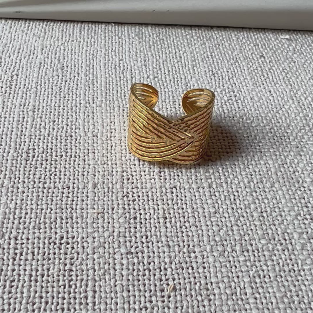Vidéo de la bague Avenir ajustable, au design géométrique en acier inoxydable doré, posée sur un tissu beige texturée.