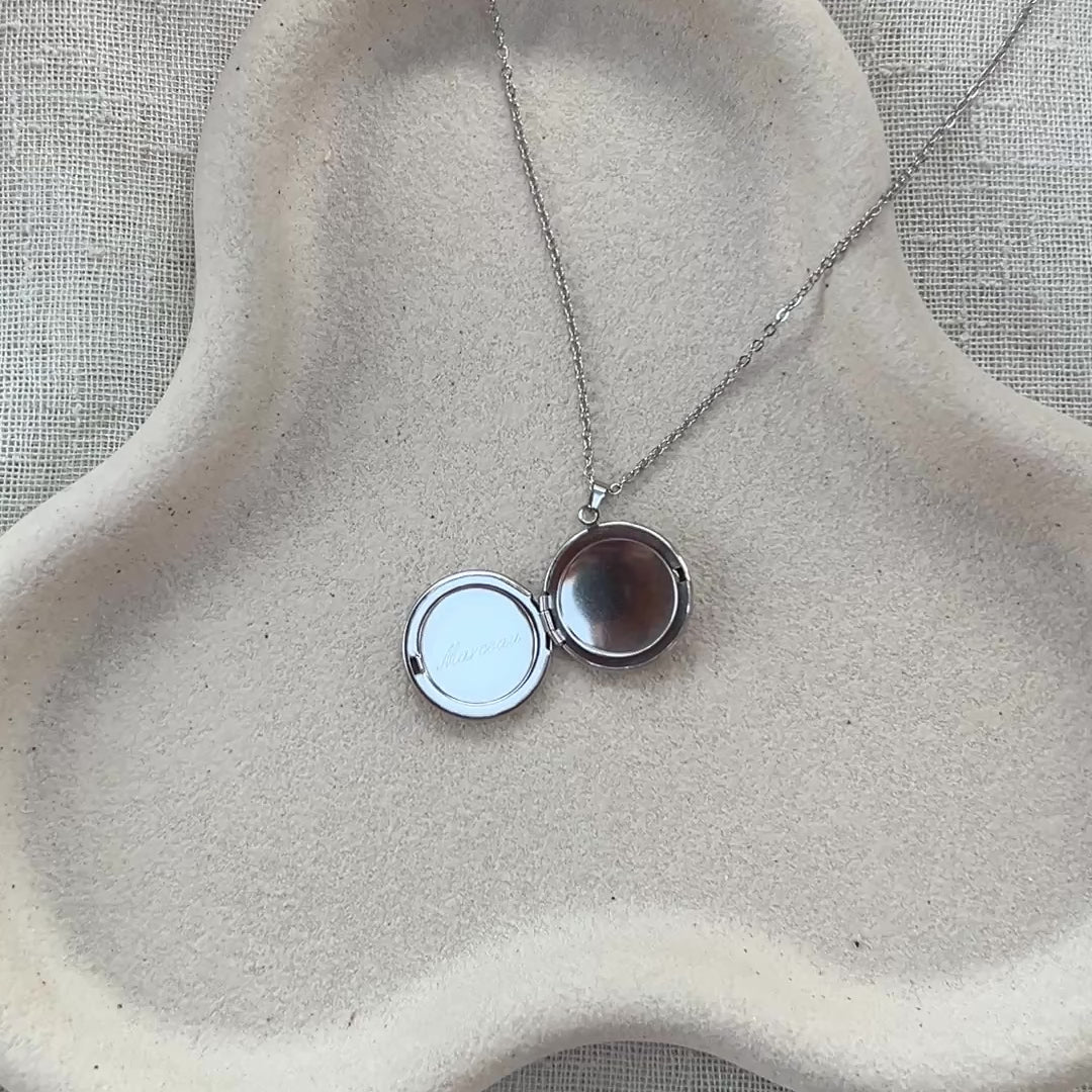 Vidéo du collier "Ce jour là" avec médaillon rond personnalisable en acier argenté, présenté sur un fond beige texturé, gravé du prénom Marceau. 