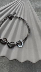Vidéo du bracelet "Emotive" en acier argenté, orné de trois cœurs mobiles, posé sur un fond beige texturé.